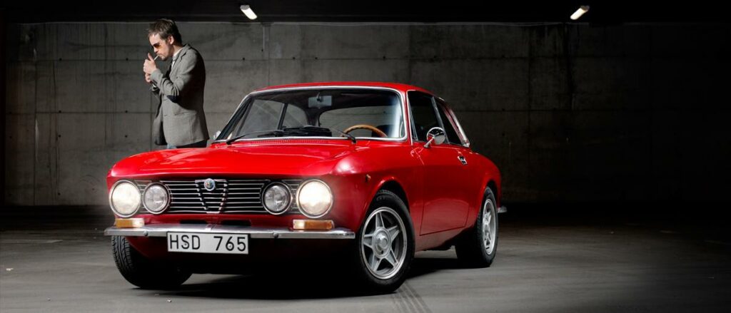 En man i kostym står bredvid en röd bil. (AI text)