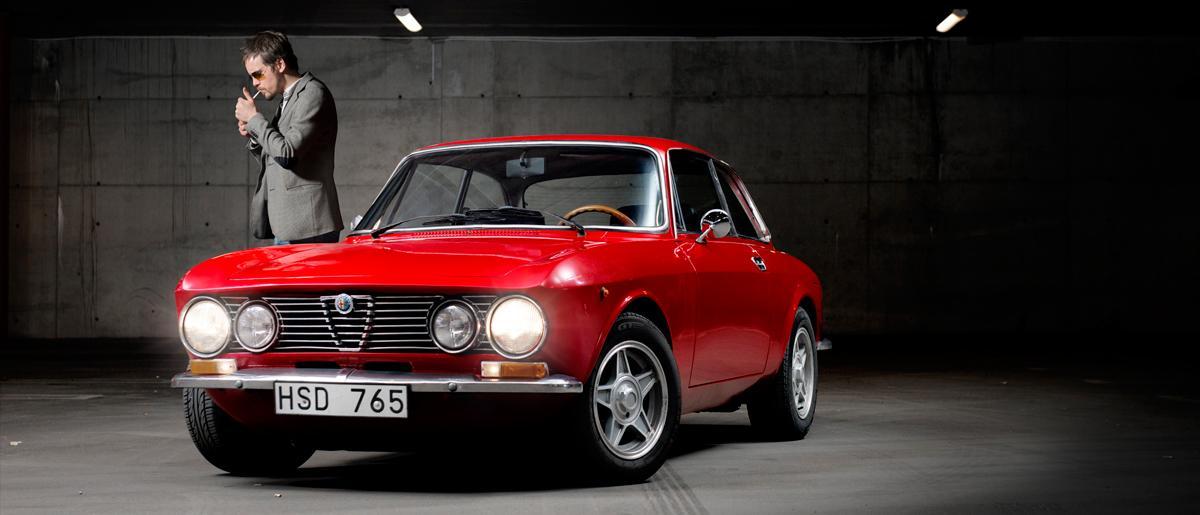 En man i kostym står bredvid en röd bil. (AI text)