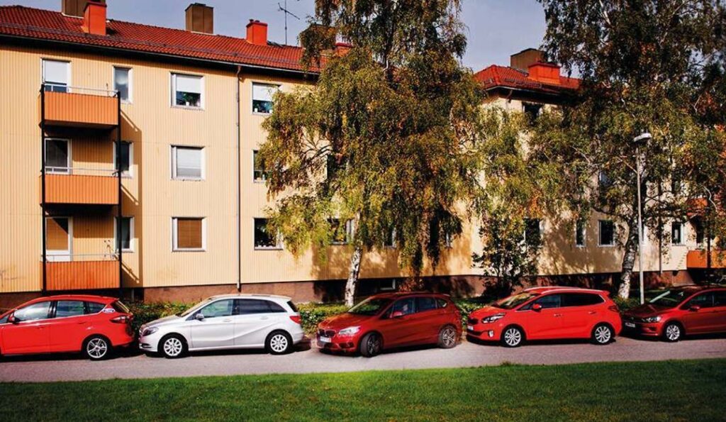 En grupp bilar parkerade framför ett byggnad. (AI text)