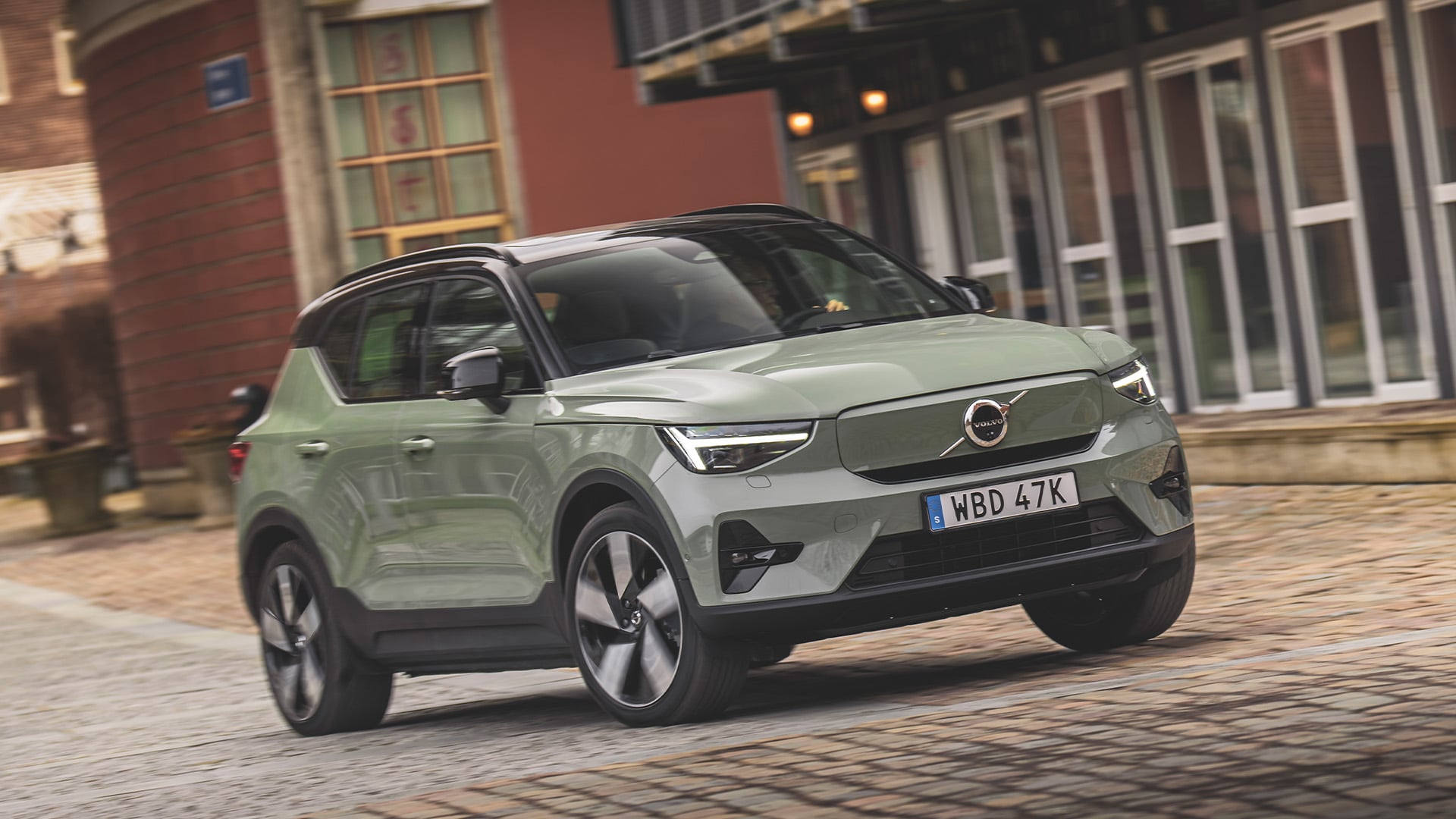 Mossgrön Volvo XC40 snett framifrån kör i stadsmiljö.