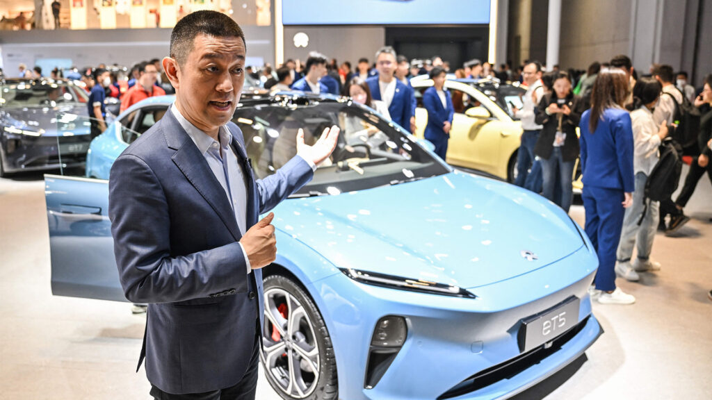 En man står bredvid en blå bil på Shanghais bilsalong. Bild: Reuters (AI text)