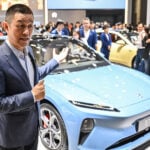 En man står bredvid en blå bil på Shanghais bilsalong. Bild: Reuters (AI text)