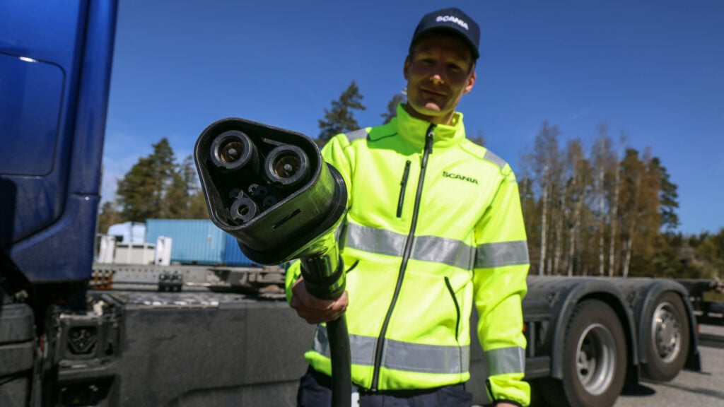 En lastbilsförare i ett gult västar står bredvid en blå lastbil. (AI text)