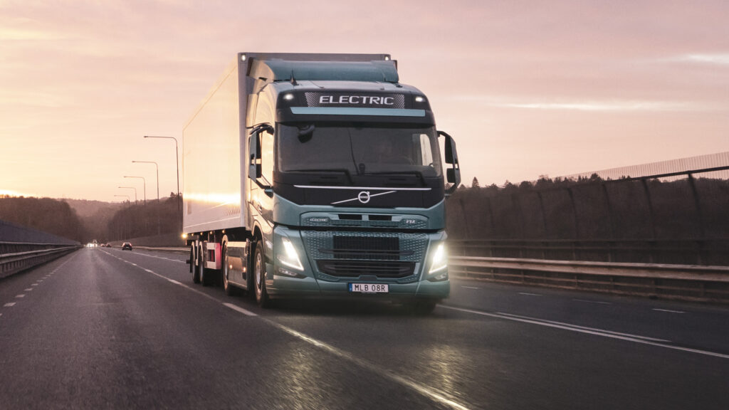 En Volvo-lastbil kör längs en motorväg vid solnedgången. (AI text)