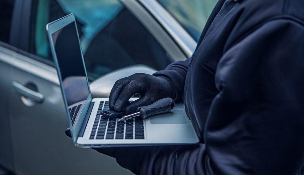 En man i svart jacka håller en laptop och en bilnyckel. (AI text)