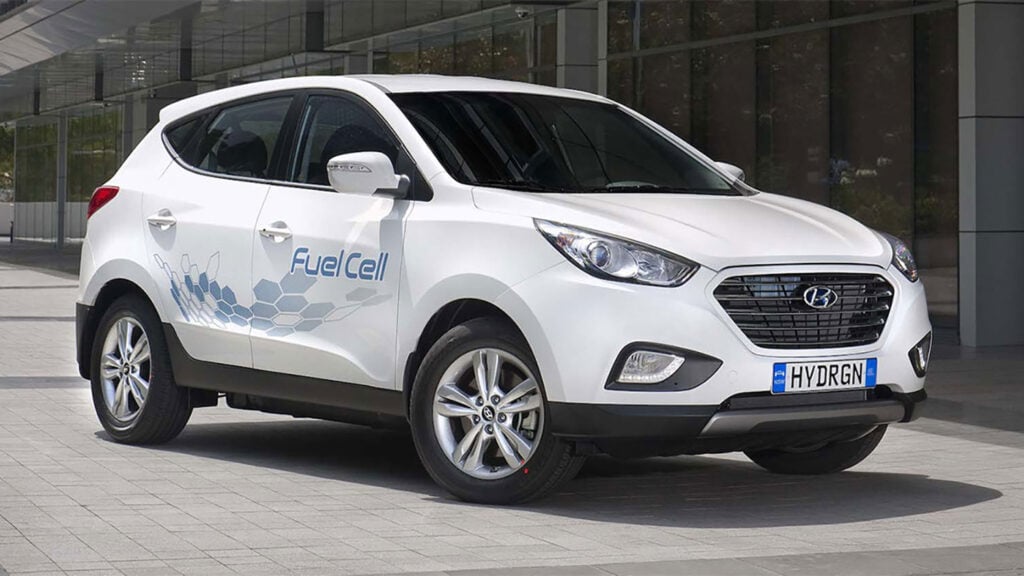 En vit Hyundai Tucson parkerad framför ett byggnad. (AI text)