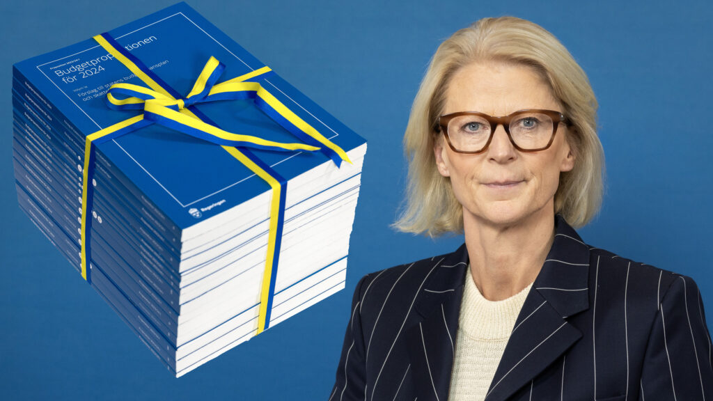 En kvinna med glasögon står bredvid en stapel böcker. (AI text)