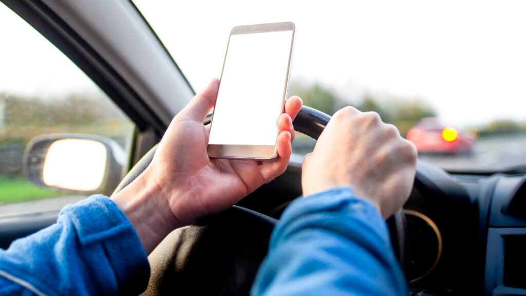 En man kör en bil samtidigt som han använder en mobiltelefon. (AI text)