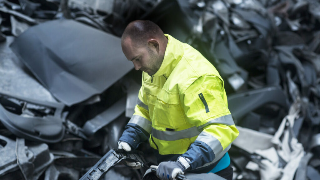 En man tar bort en bil från en hög skrotmetall. (AI text)