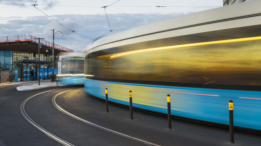 En blå och vit spårvagn kör nerför en gata. (AI text)