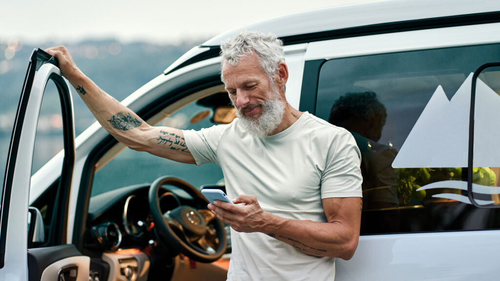 En man står bredvid en lättlastare och tittar på sin mobiltelefon. (AI text)