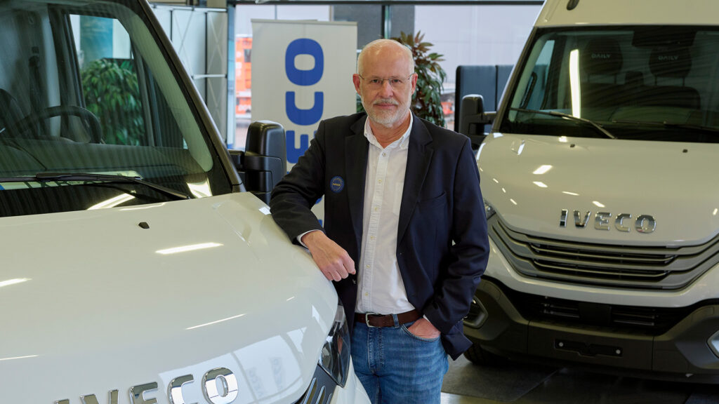 En man står bredvid en vit fraktrut. (AI text)