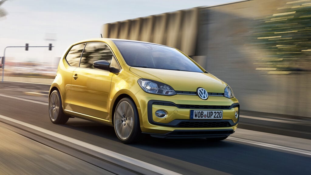 En gul Volkswagen up! kör nerför en stadsgata. (AI text)