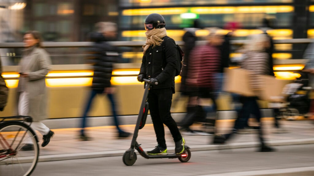 En kvinna cyklar på en scooter i staden. (AI text)