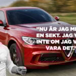 En man kör en röd bil med någon i bakgrunden. (AI text)