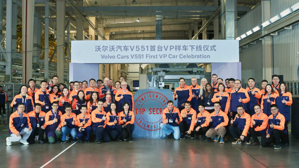 En grupp personer poserar för en foto i en fabrik. (AI text)