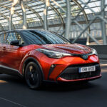 Orange Toyota C-HR på väg snett framifrån.
