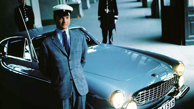 En man i kostym står bredvid en klassisk bil. (AI text)