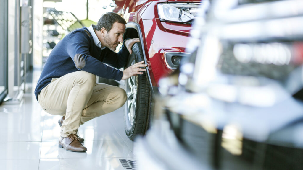 En man knäler ned för att inspektera en bil i en showrum. (AI text)