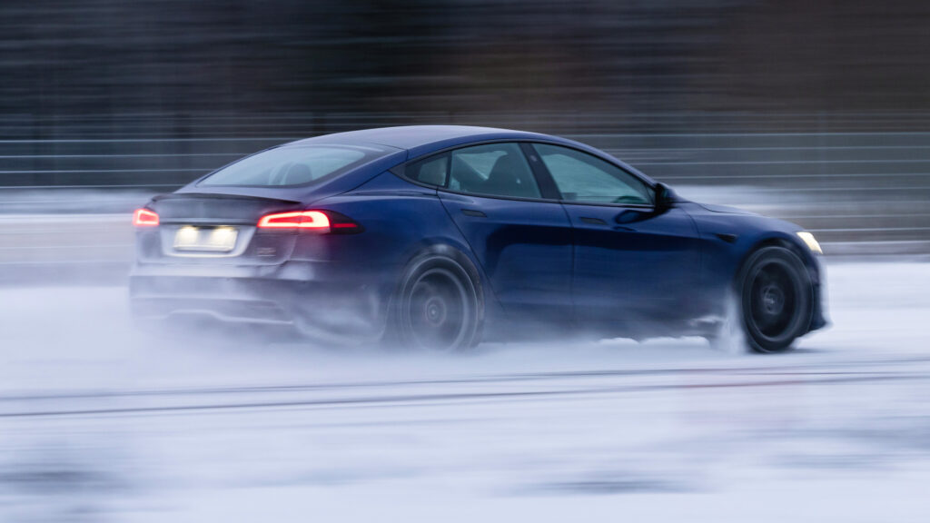 En blå bil kör på en snöig bana. (AI text)