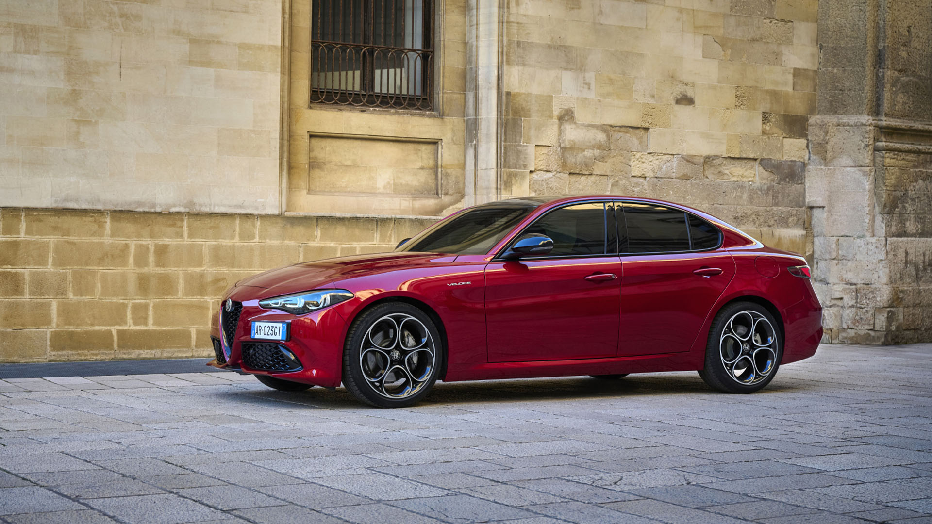 Röd Alfa Romeo Giulia med en italiensk tegelfasad bakom.