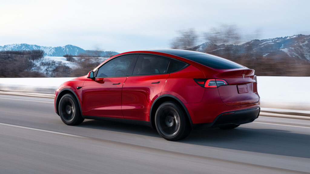 En röd Tesla Model Y kör nerför en snötäckt väg. (AI text)