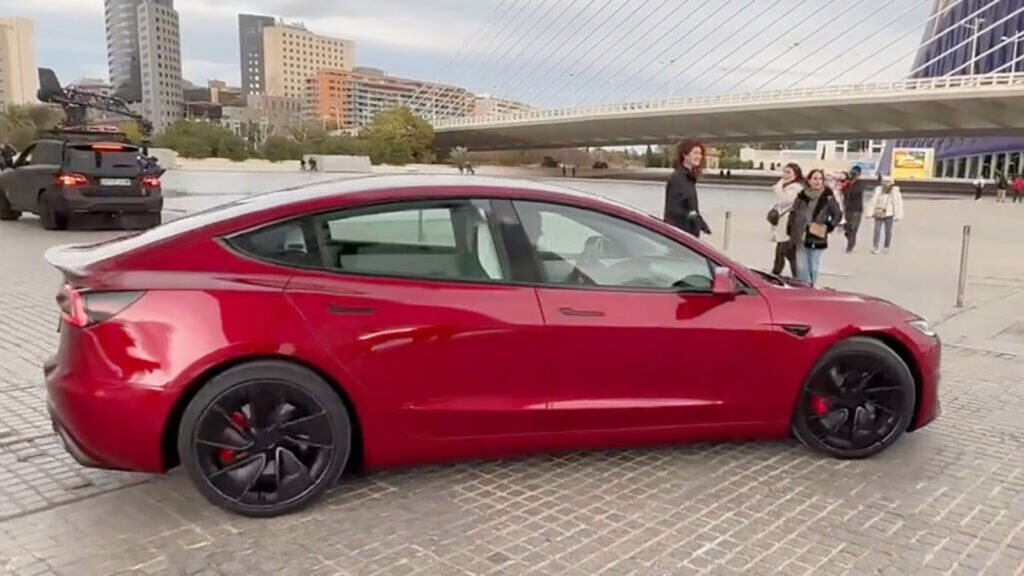 Tesla Model 3 parkerad framför en bro (AI text)