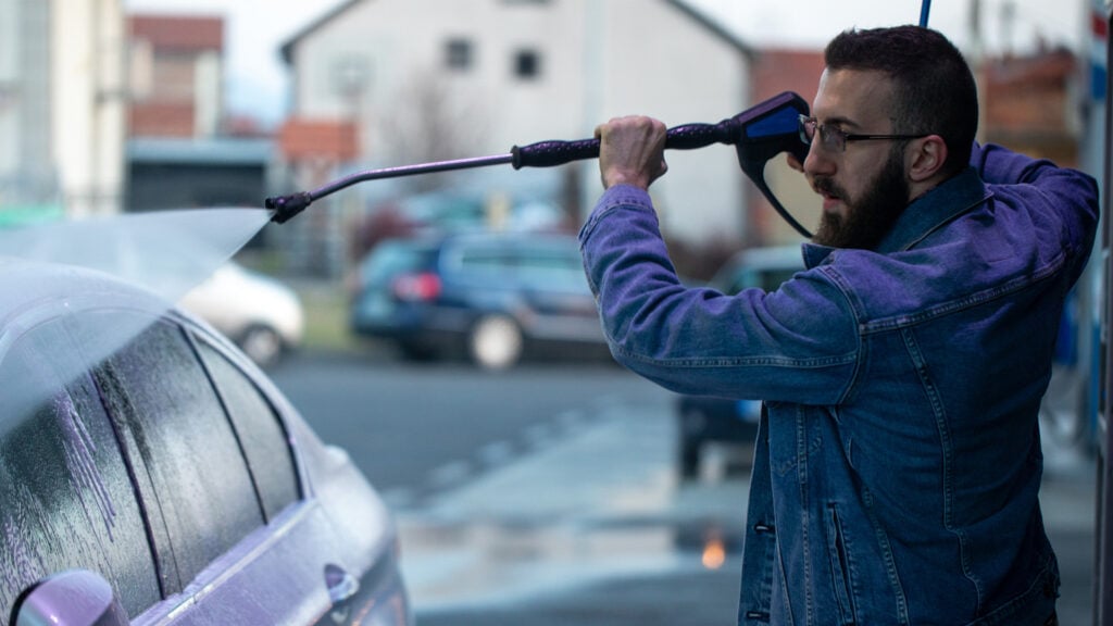 En man tvättar sin bil med en tryckrengörare. (AI text)
