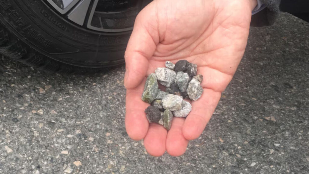 En person håller en haften stenar framför en bil. (AI text)