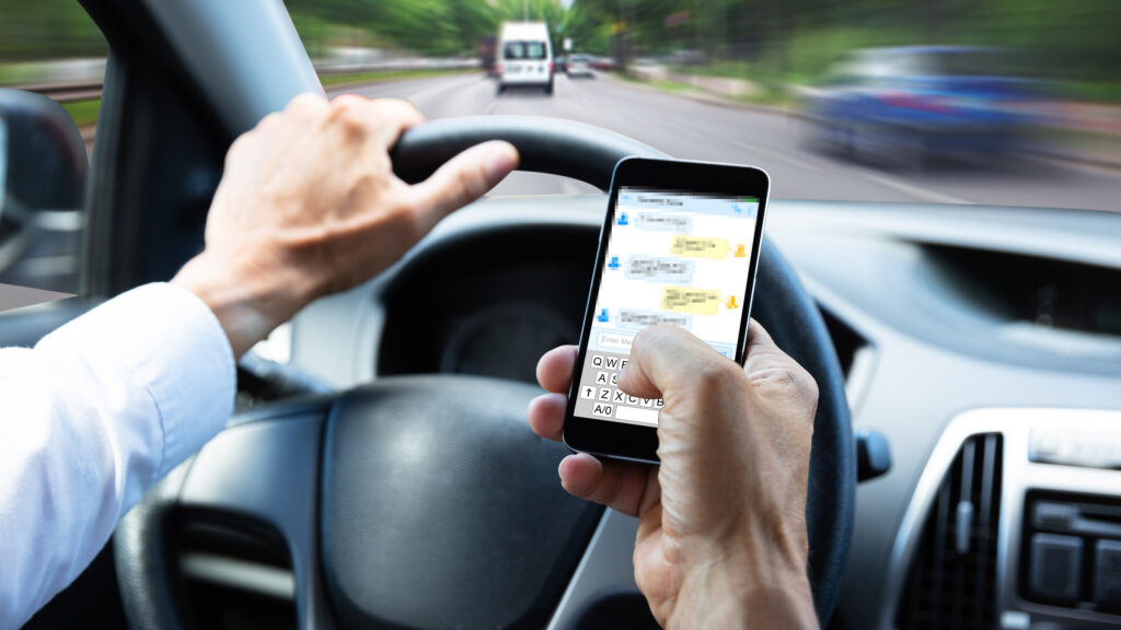 En man kör en bil samtidigt som han använder sin telefon. (AI text)