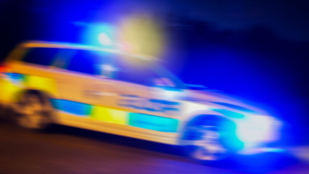 En polisbil kör nedför en väg på natten. (AI text)