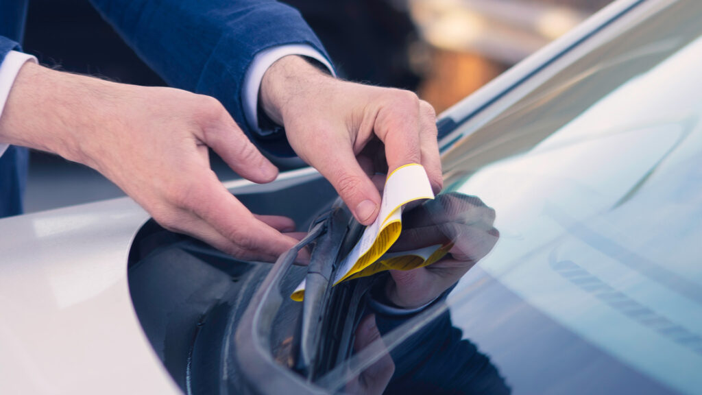 En man sätter en etikett på vindrutan av en bil. (AI text)