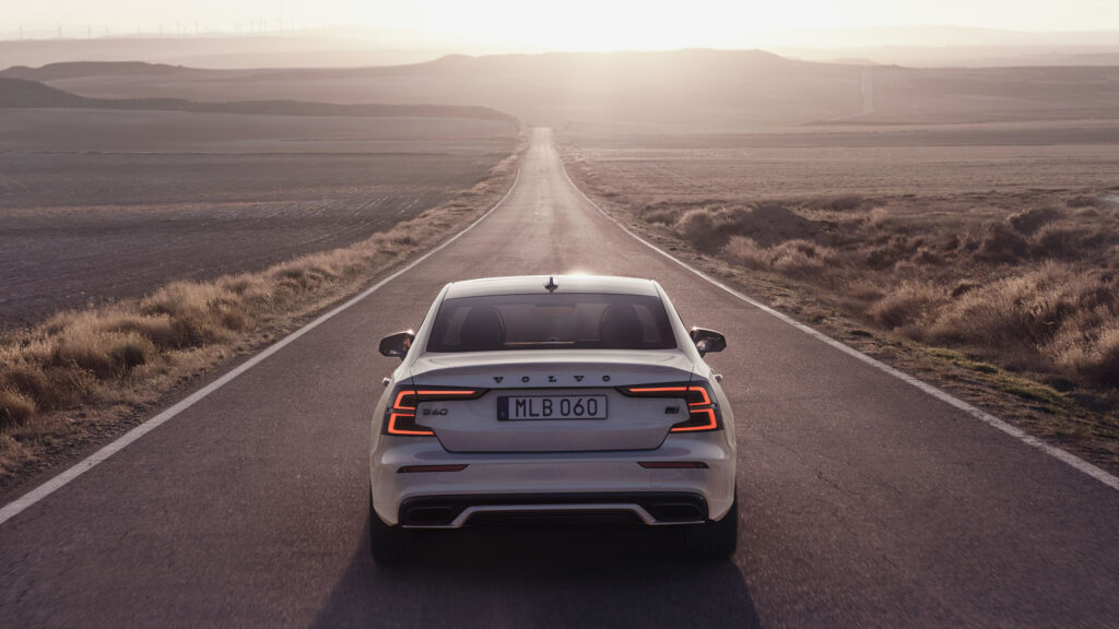 En vit Volvo XC90 kör nedför en landsväg vid solnedgången. (AI text)