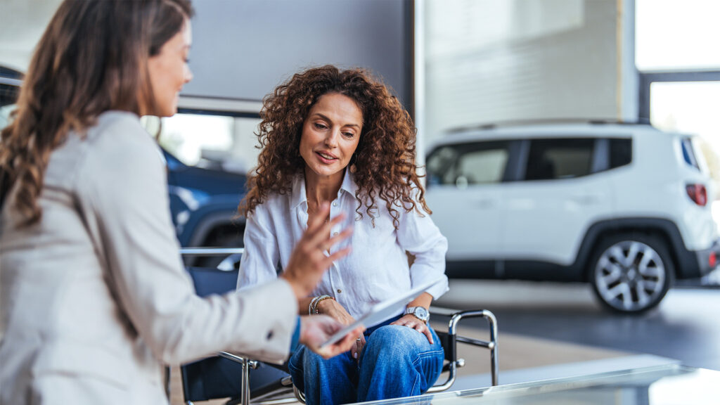 En kvinna och en man pratar om bilar i en showrum. (AI text)