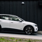 En vit SUV parkerad framför ett svart hus. (AI text)