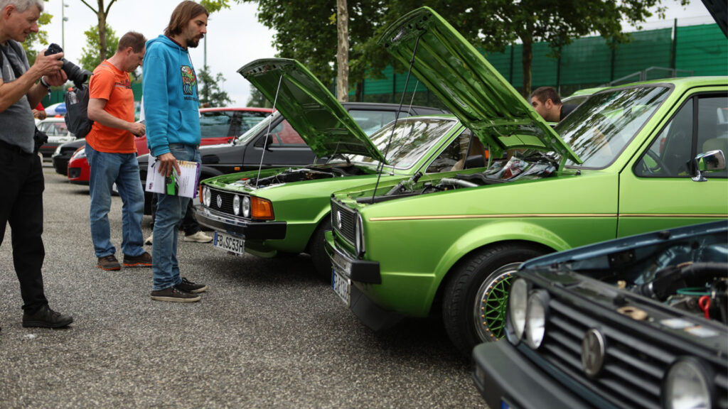 En grupp personer står omkring en grön bil. (AI text)