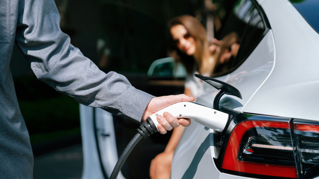 En man laddar sin Tesla Model S elbil. (AI text)