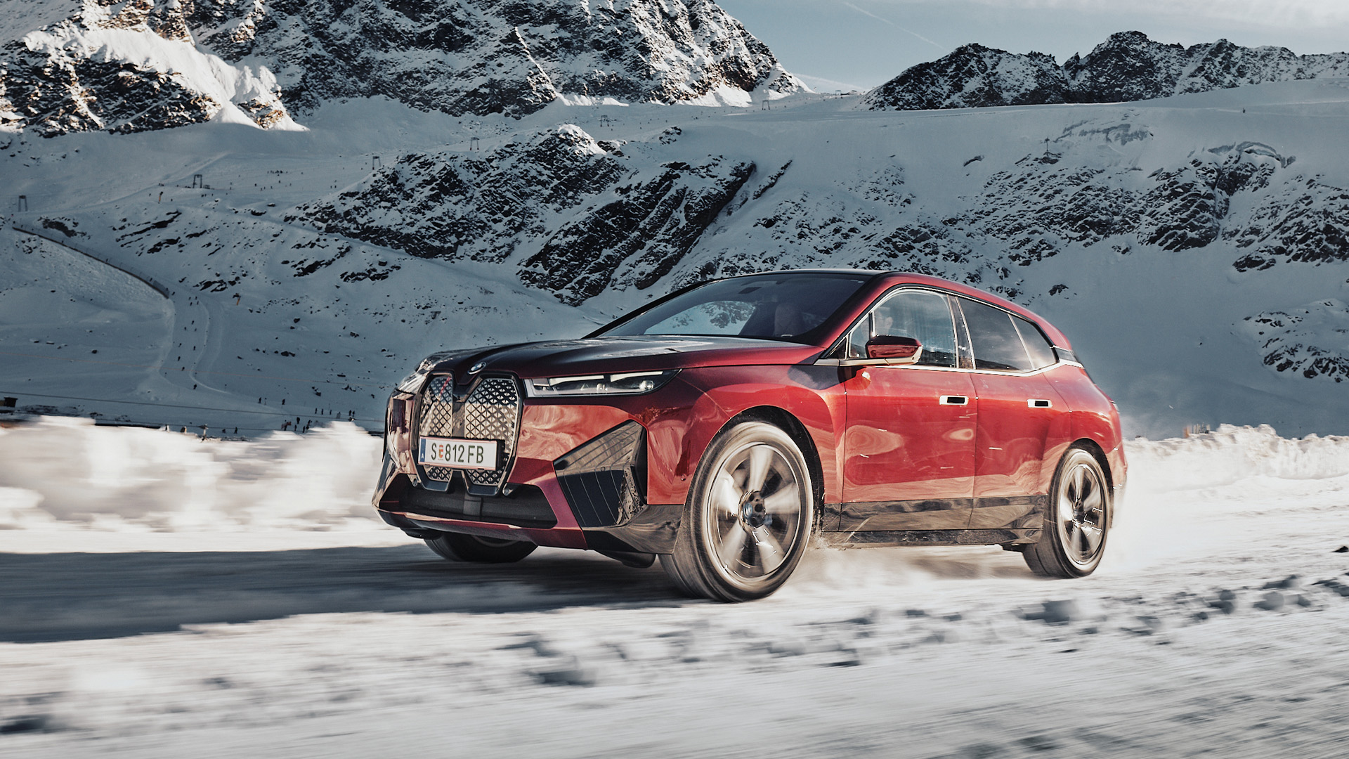 Vinröd BMW iX kör i snölandskap med snötäckta berg i bakgrunden.