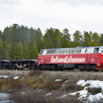 En tåg rullar längs spåret intill en flod. (AI text)