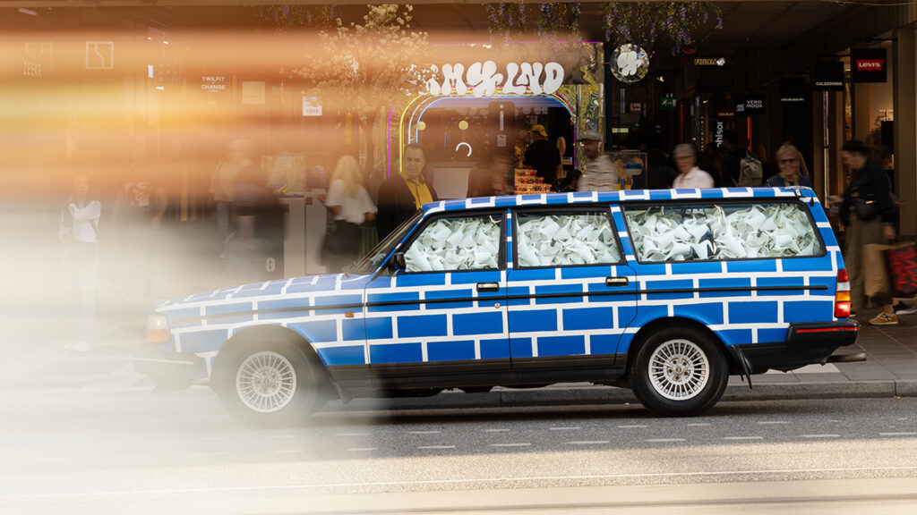 En blå och vit bil med en mur bredvid. (AI text)