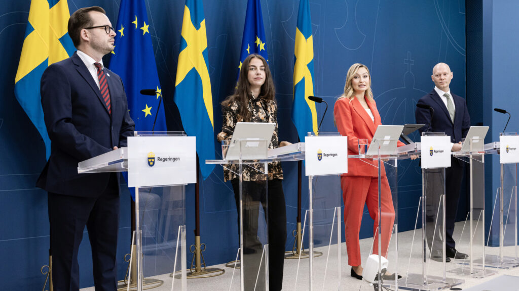 En grupp personer står vid pultar framför en flagga. (AI text)