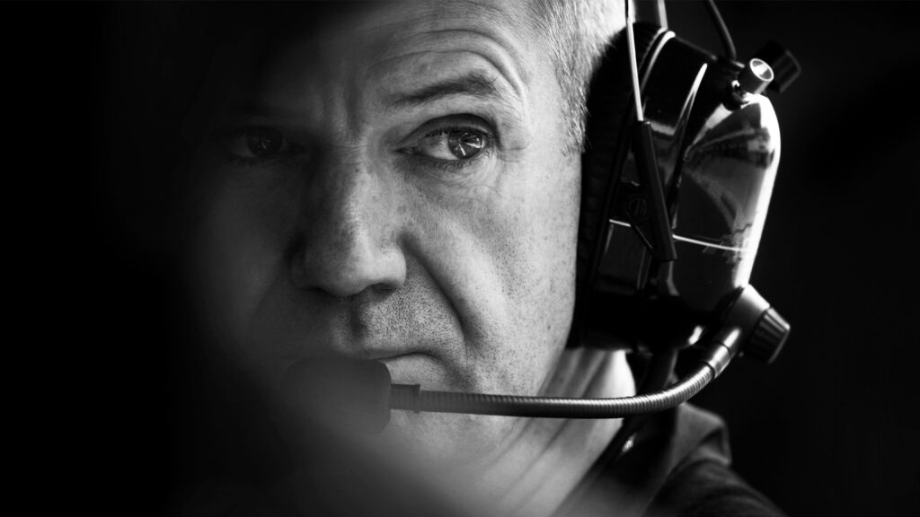 En man med huvudtelefon sits framför kameran. (AI text)