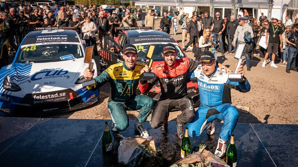 En grupp personer står på en podiet med sina bilar i bakgrunden. (AI text)