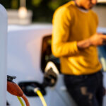 En man laddar sin elbil på en laddstation. (AI text)