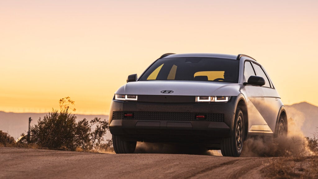 En vit SUV kör nedför en grusväg vid solnedgång. (AI text)