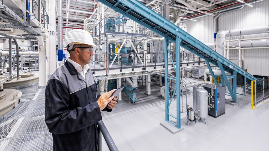 En man står i en fabrik och tittar på en konvoyrörband. (AI text)