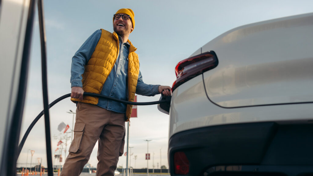 Man med mössa och dunväst laddar vit elbil.