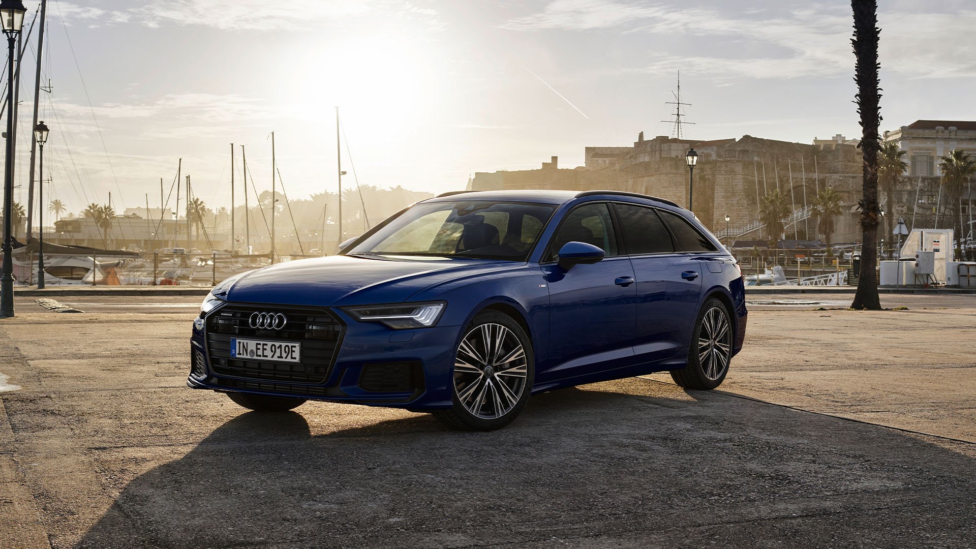 Blå Audi A6 Avant med hamn och solnedgång i bakgrunden.