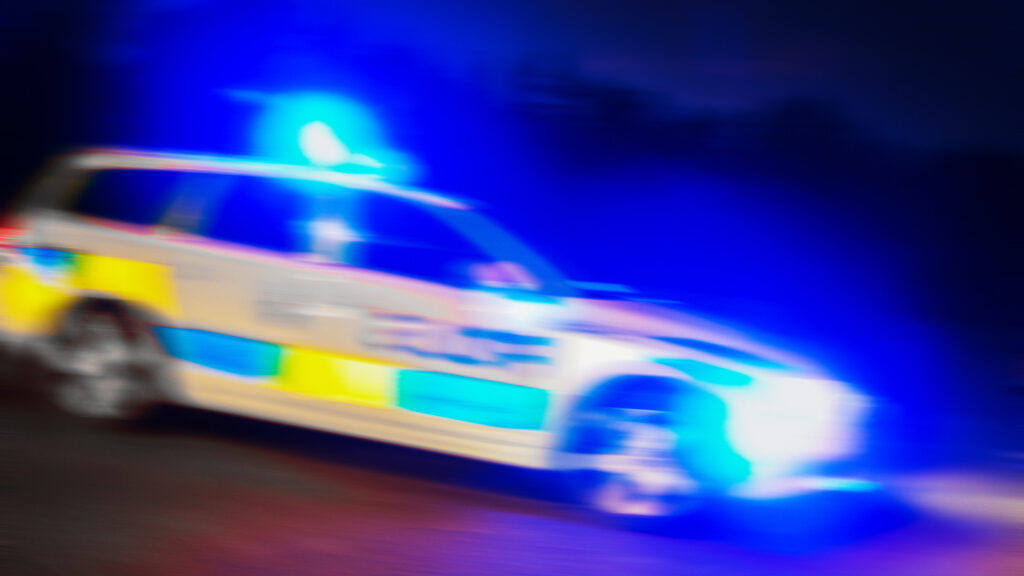 En polisbil kör ner en gata på natten. (AI text)