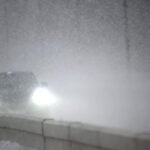 Bilar kör längs väg i snöoväder.